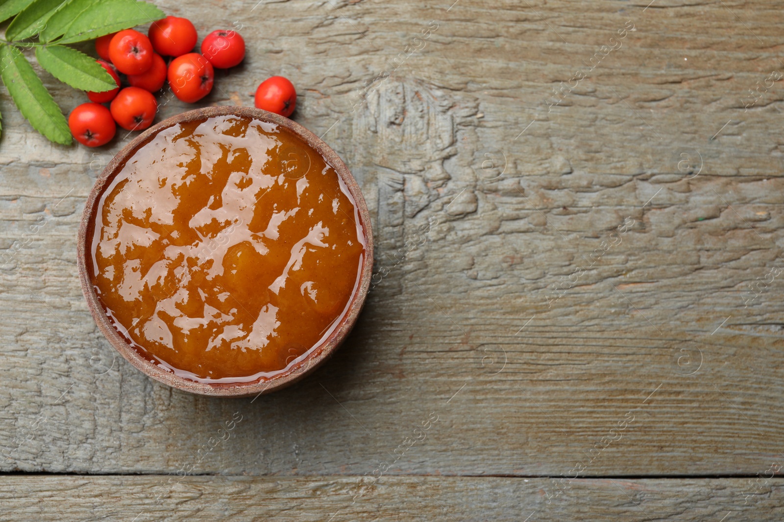 Photo of Delicious rowan jam and berries on wooden table, flat lay. Space for text