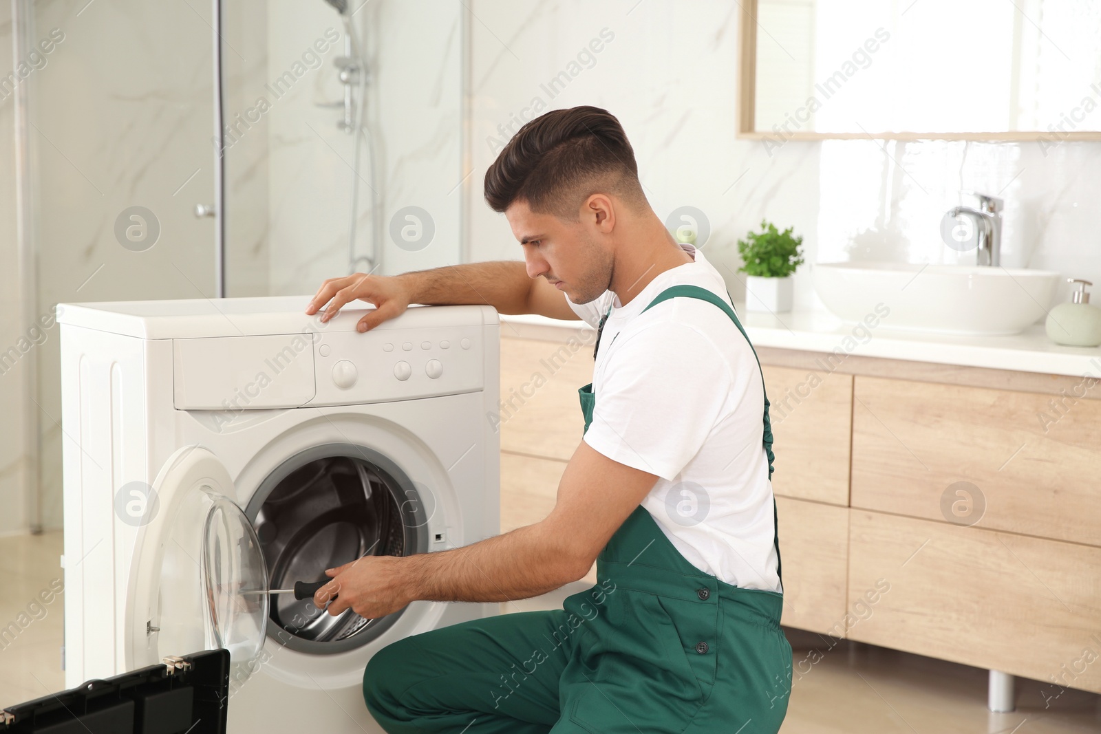 Photo of Professional plumber repairing washing machine in bathroom