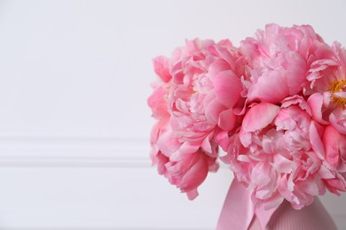 Beautiful bouquet of pink peonies in vase near white wall, closeup. Space for text