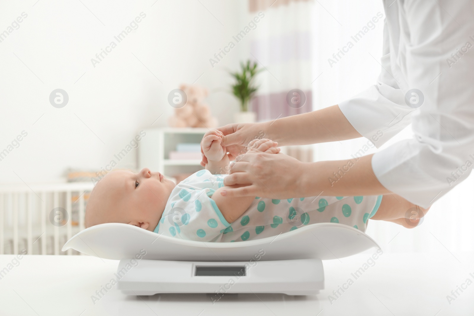 Photo of Doctor weighting baby on scales in light room