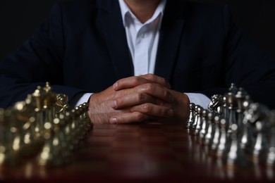 Photo of Man with chess pieces on board before game against dark background, closeup