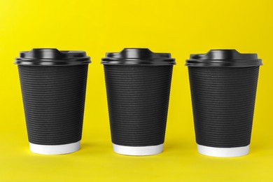 Photo of Paper cups with black lids on yellow background. Coffee to go