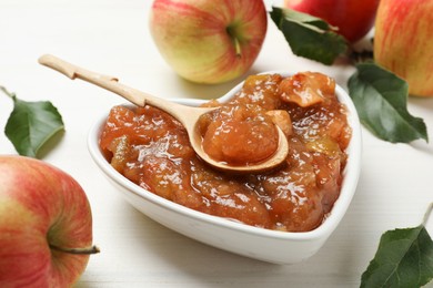 Photo of Tasty apple jam in heart shaped bowl and fresh fruits on white wooden table, closeup