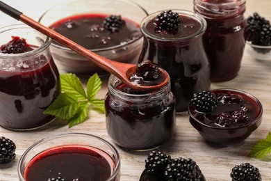 Photo of Taking tasty blackberry jam with spoon on white wooden table