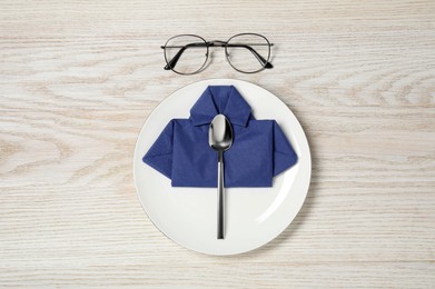 Photo of Plate with shirt made of paper napkin, spoon and glasses on wooden table, flat lay. Business lunch concept