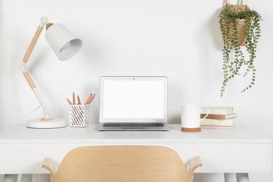 Photo of Cozy workspace with laptop, lamp and stationery on wooden desk at home