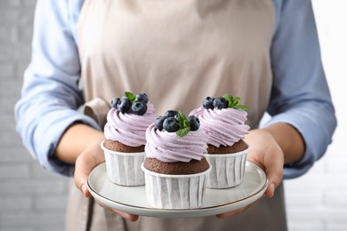 Photo of Woman holding plate with sweet cupcakes, closeup