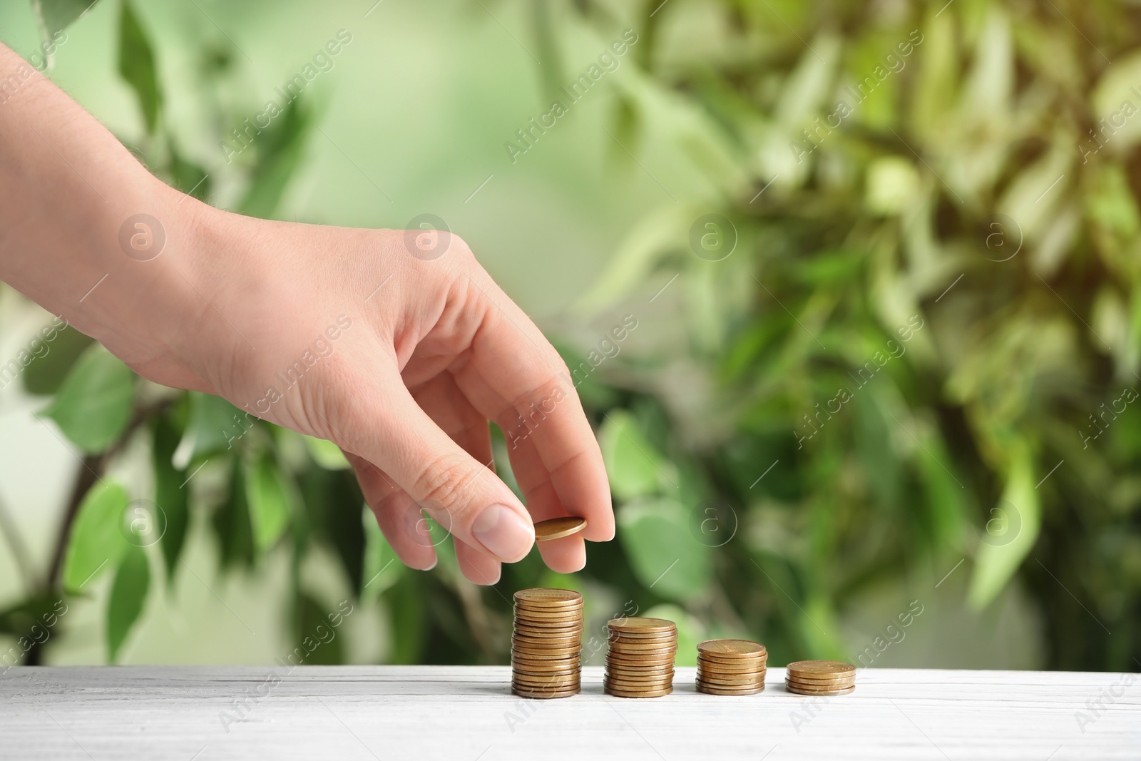 Photo of Woman stacking coins on white wooden table against blurred background, closeup. Money savings