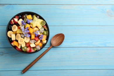 Photo of Delicious exotic fruit salad and spoon on light blue wooden table, flat lay. Space for text