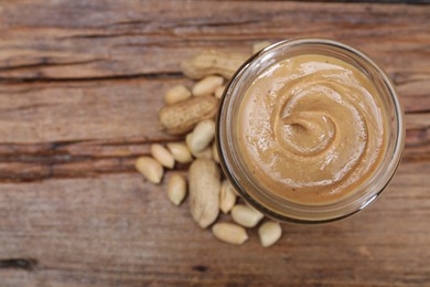 Tasty peanut nut paste in jar on wooden table, top view. Space for text