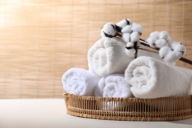 Photo of Rolled soft towels and cotton branch on white table indoors, space for text
