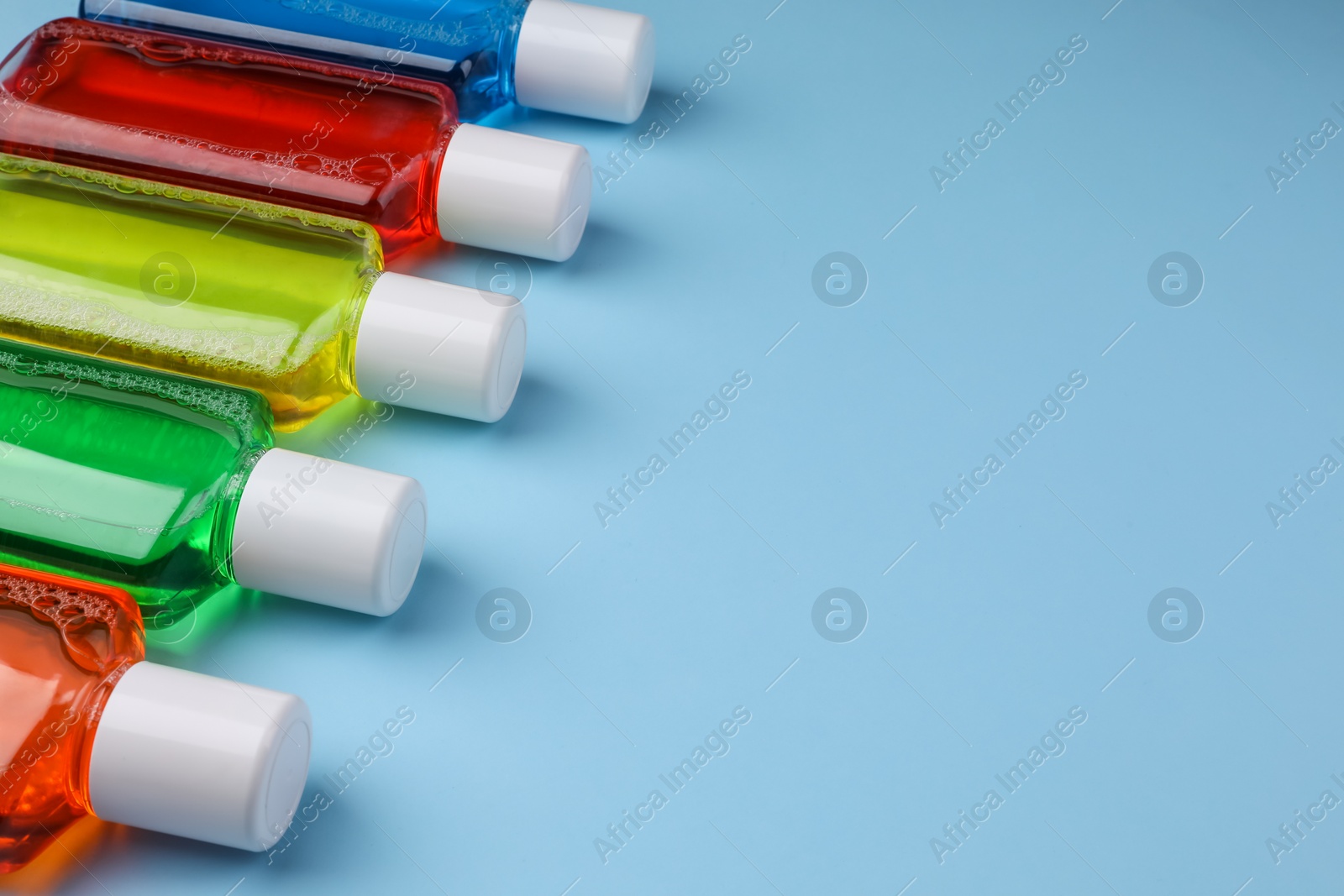 Photo of Fresh mouthwashes in bottles on light blue background, closeup. Space for text