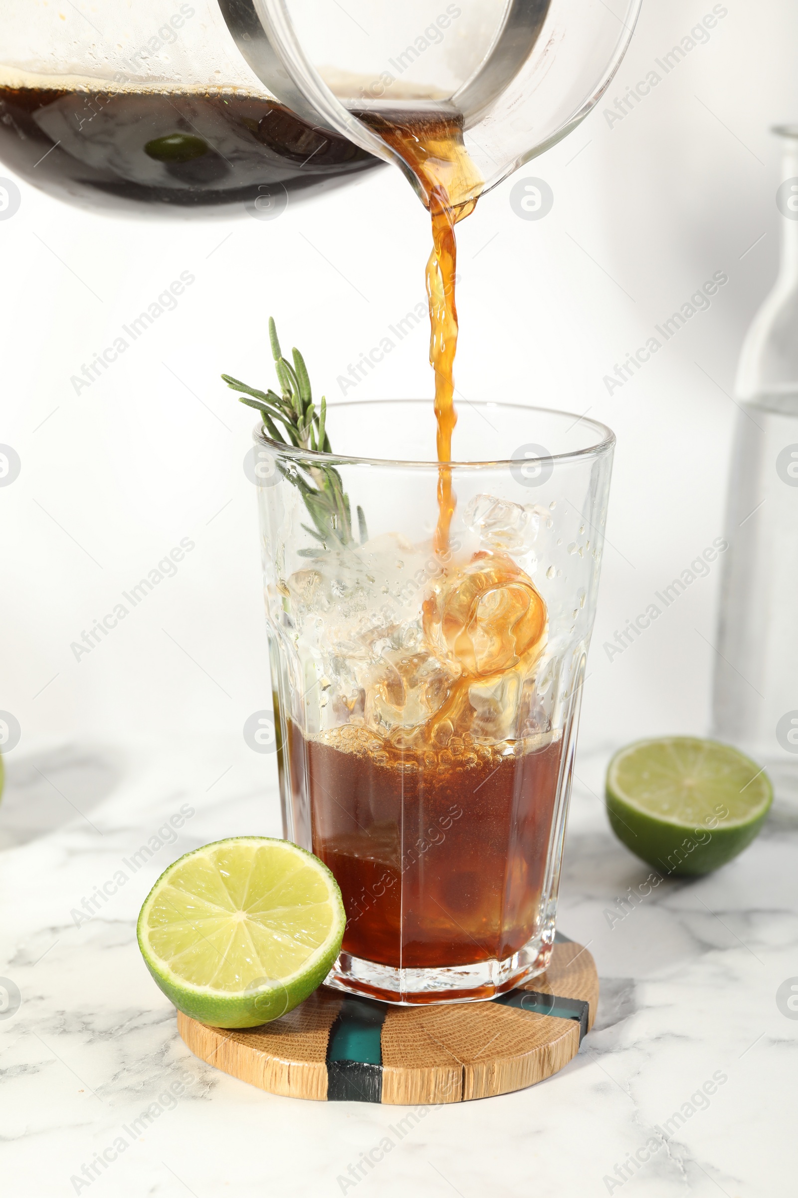 Photo of Pouring coffee into glass with ice cubes at white marble table