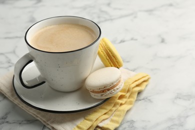 Photo of Tasty cappuccino in cup, macarons and saucer on white marble table, closeup. Space for text