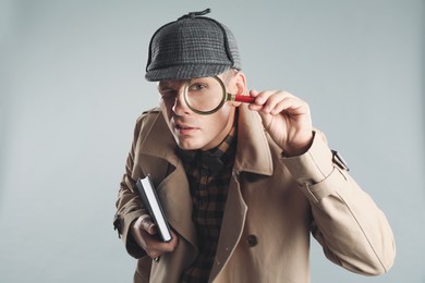 Photo of Male detective looking through magnifying glass on grey background