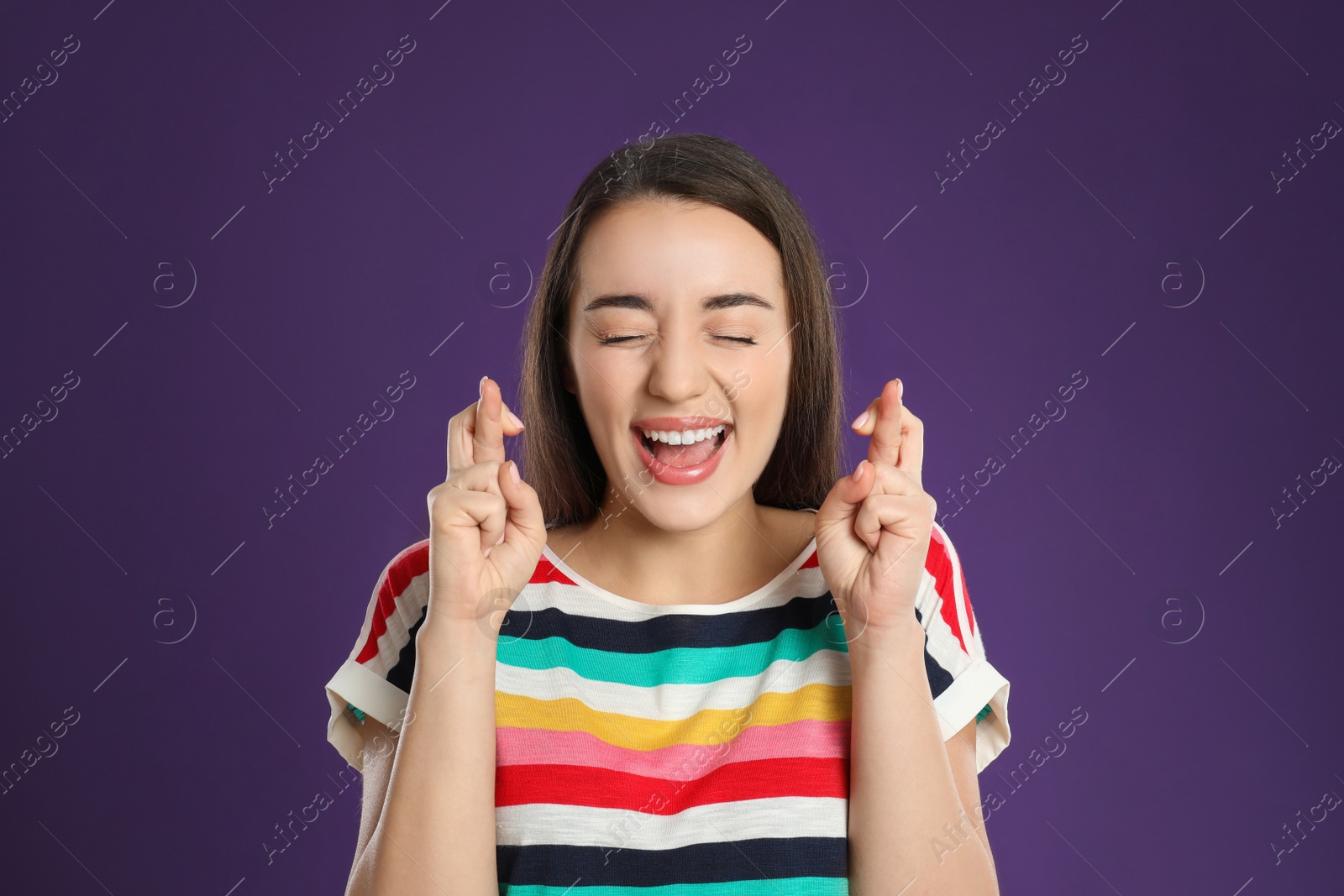 Photo of Woman with crossed fingers on purple background. Superstition concept