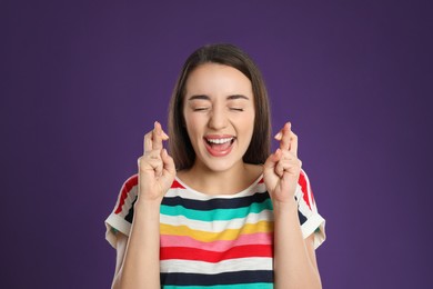 Photo of Woman with crossed fingers on purple background. Superstition concept