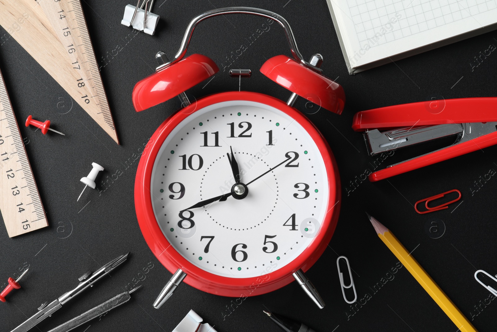 Photo of Flat lay composition with alarm clock and different stationery on black background. School time