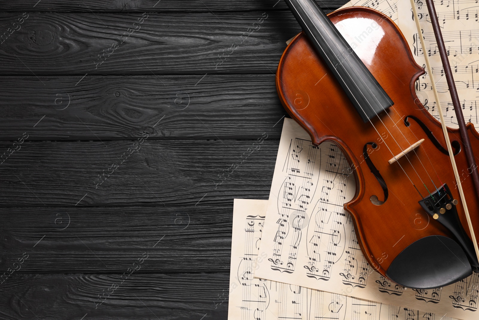 Photo of Violin, bow and music sheets on black wooden table, top view. Space for text