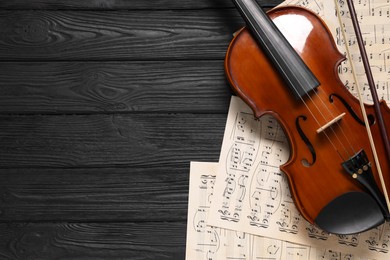 Violin, bow and music sheets on black wooden table, top view. Space for text