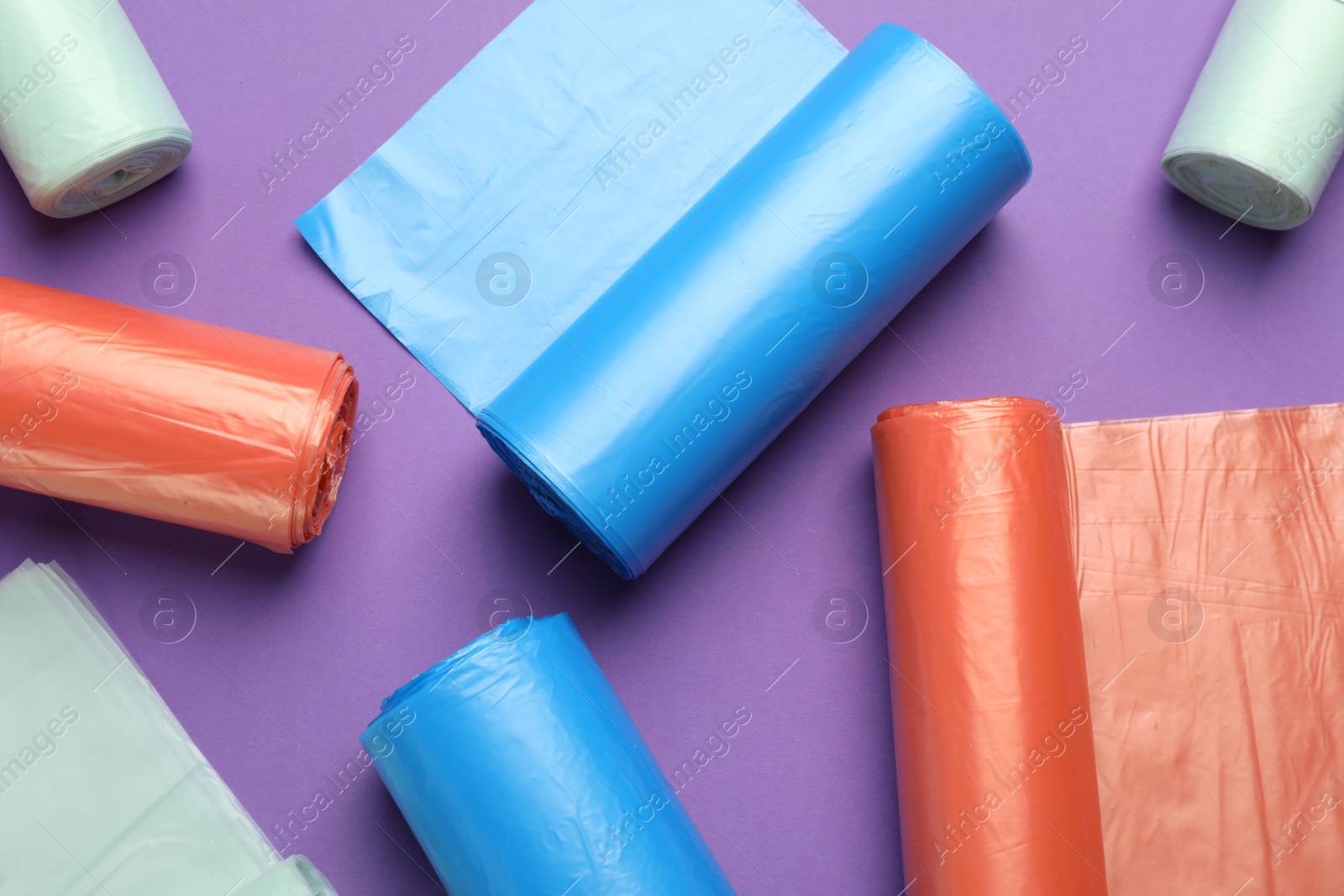 Photo of Rolls of different color garbage bags on violet background, flat lay