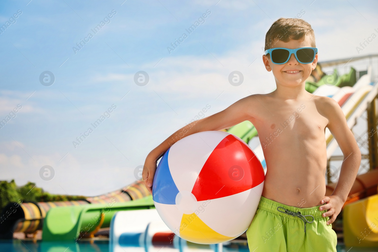 Photo of Cute little boy with inflatable ball near pool in water park, space for text