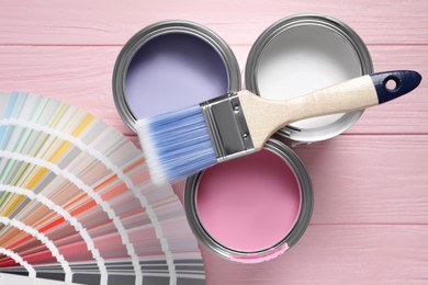 Photo of Cans of pastel paints, palette and brush on pink wooden table, flat lay