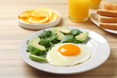 Photo of Plate of fried egg with avocado and spinach on wooden table. Healthy breakfast