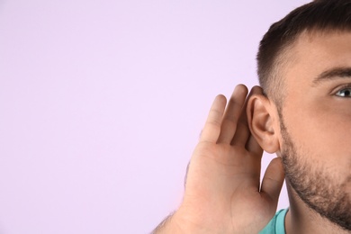 Young man with hearing problem on color background with copy space text, closeup