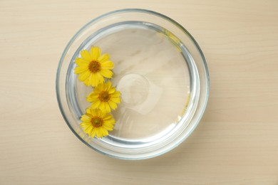 Photo of Glass bowl with water and yellow flowers on wooden table, top view