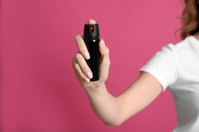 Young woman using pepper spray on pink background, closeup
