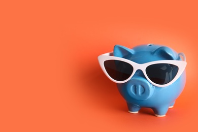 Piggy bank with sunglasses on color background, space for text. Travel agency