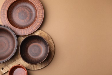 Photo of Ceramic bowls, wooden board and plate on beige background, flat lay. Space for text