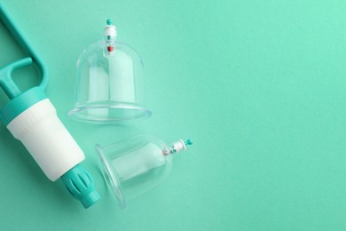 Photo of Plastic cups and hand pump on turquoise background, flat lay with space for text. Cupping therapy