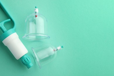 Plastic cups and hand pump on turquoise background, flat lay with space for text. Cupping therapy