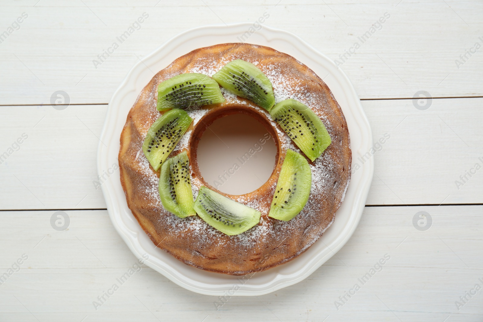 Photo of Homemade yogurt cake with kiwi and powdered sugar on white wooden table, top view