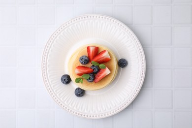 Delicious pancakes with strawberries, blueberries and mint on white tiled table, top view