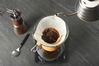 Pouring hot water into glass chemex coffeemaker with paper filter and coffee on gray table, above view