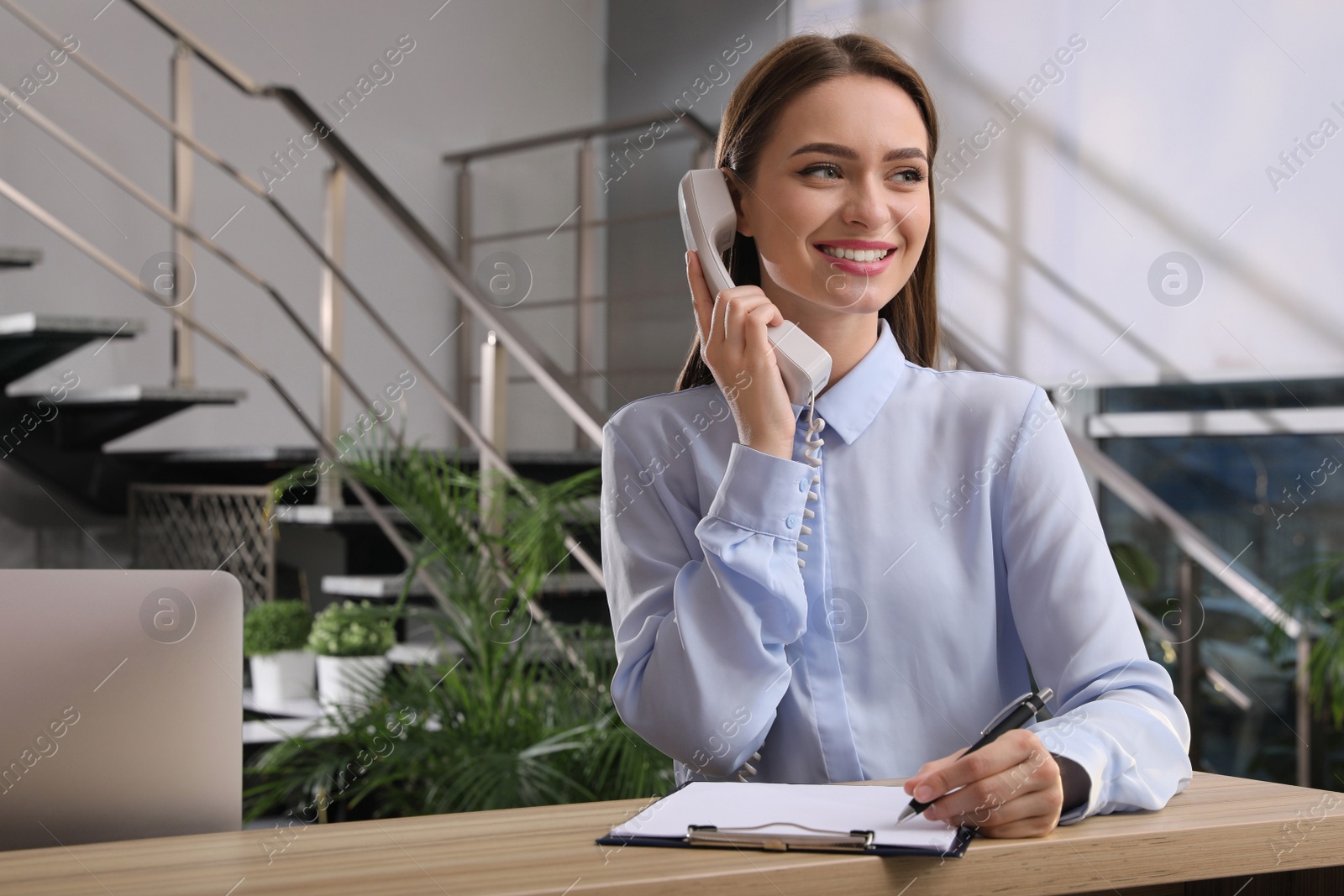Photo of Female receptionist with clipboard talking on phone at workplace. Space for text
