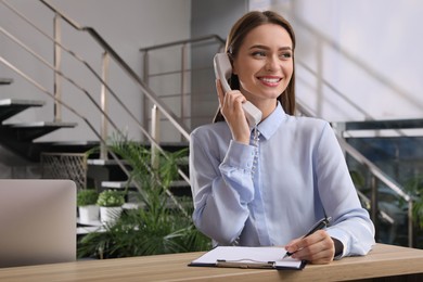 Photo of Female receptionist with clipboard talking on phone at workplace. Space for text