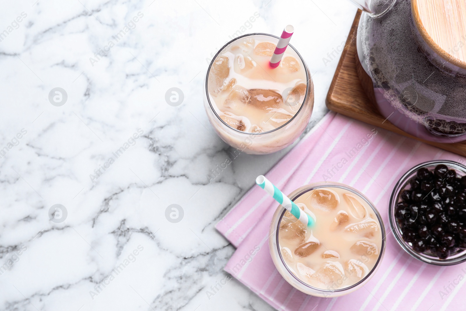 Photo of Bubble milk tea and bowl with tapioca balls on white marble table, flat lay. Space for text