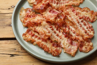 Photo of Delicious fried bacon slices on wooden table, closeup
