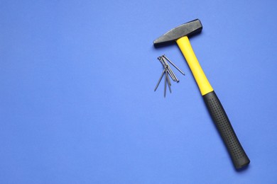 Photo of Hammer and metal nails on blue background, top view. Space for text