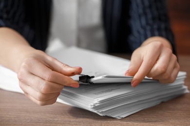 Woman attaching documents with metal binder clip at wooden table in office, closeup