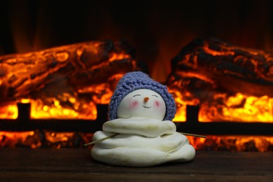 Cute decorative snowman in hat on wooden floor near fireplace