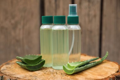 Photo of Bottles of cosmetic products and sliced aloe vera leaves on wooden stump