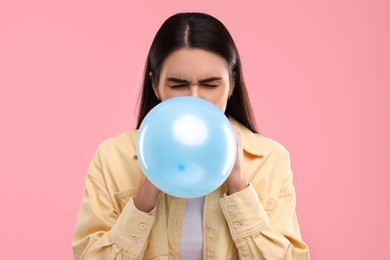 Photo of Woman inflating light blue balloon on pink background