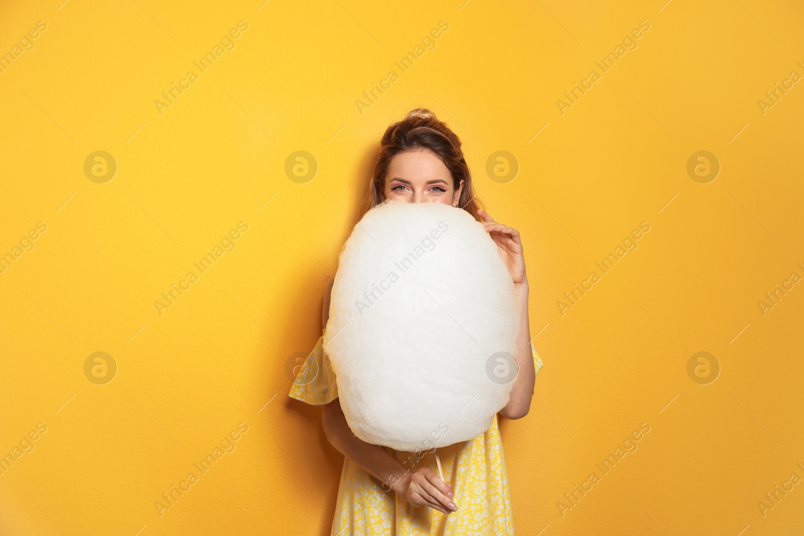 Photo of Young woman with tasty cotton candy on yellow background