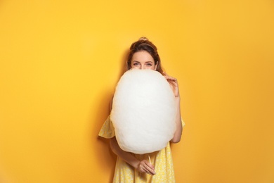 Young woman with tasty cotton candy on yellow background