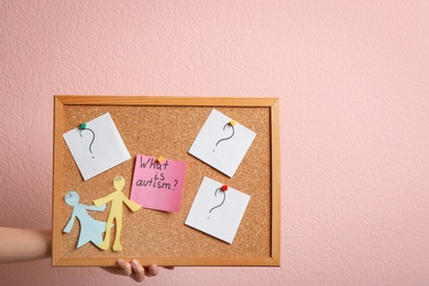 Photo of Woman holding board with phrase "What is autism?" and paper figures on color background